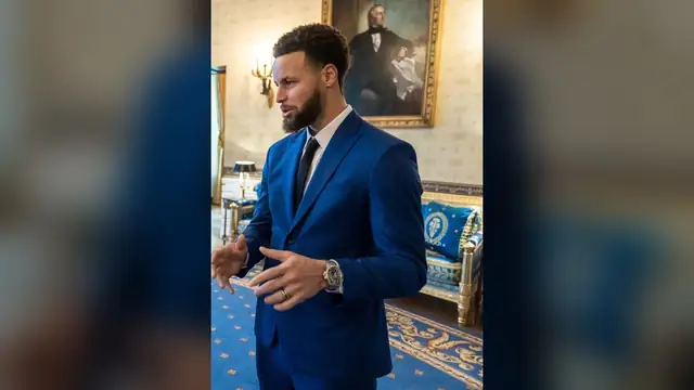 Stephen Curry in a royal blue suit gestures as he talks in the Blue Room of the White House during the Warriors' championship visit in January 2023