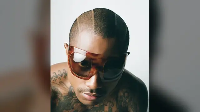 Steve Lacy in oversized tortoiseshell sunglasses looking down at the camera against a pale studio backdrop