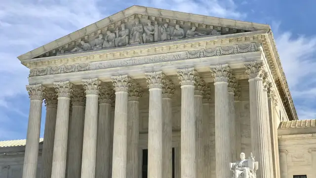 The white marble front of the U.S. Supreme Court building with its tall columns and seated statue under a blue sky