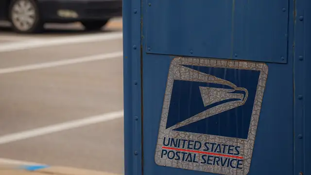 A weathered blue United States Postal Service mailbox stands on a street corner