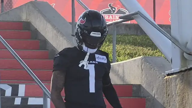 Tank Dell in a black Texans No. 1 practice jersey and helmet walks down red stadium steps at Houston Texans training camp in August 2026