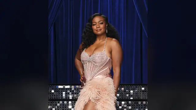 Tatyana Ali in a beaded pink corset gown with feathers posing in front of a blue velvet curtain