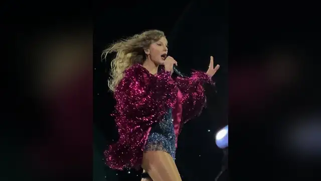 Taylor Swift singing into a microphone on stage in a sparkly pink fringed jacket