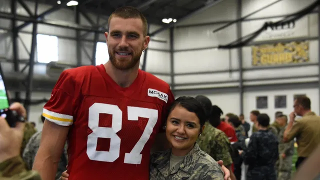 Travis Kelce in a red No. 87 Chiefs practice jersey posing with an Air National Guard airman at training camp