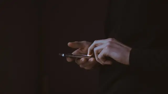 A person's hands typing on a smartphone in a dark room