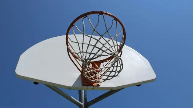 An orange basketball rim and white net viewed from below against a clear blue sky