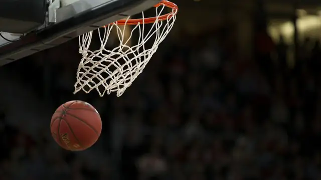 An orange basketball rests on a hardwood court floor under bright arena lights