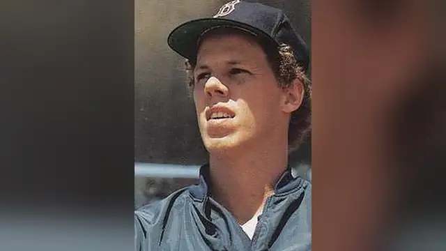A young Todd Benzinger in a navy Red Sox cap and warmup jacket looking up at a ballpark