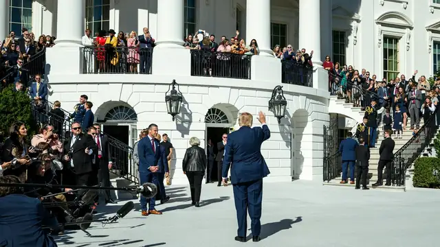 President Donald Trump waves as he walks across the White House South Lawn past a crowd watching from the balcony
