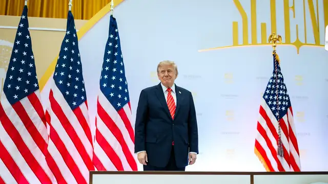 President Donald Trump stands at a podium between rows of American flags at a Washington event