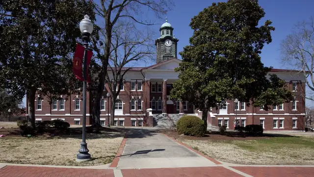 White Hall on the Tuskegee University campus in Alabama with its clock tower rising behind trees and a brick walkway
