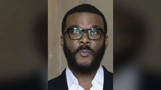 Tyler Perry in black-framed glasses with a white collared shirt and dark blazer