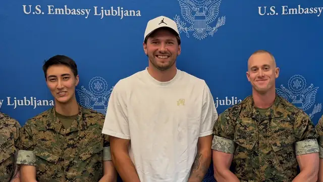 Luka Dončić in a white T-shirt and cap standing with U.S. Marines at the U.S. Embassy in Ljubljana in 2026