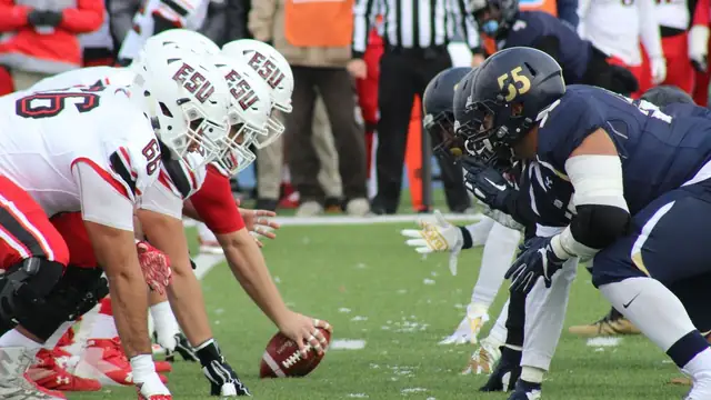 College football players lined up at the line of scrimmage on a green field in a packed stadium