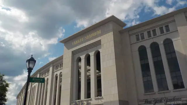 The limestone front of Yankee Stadium with its arched windows and gold Yankee Stadium lettering under a cloudy summer sky in the Bronx