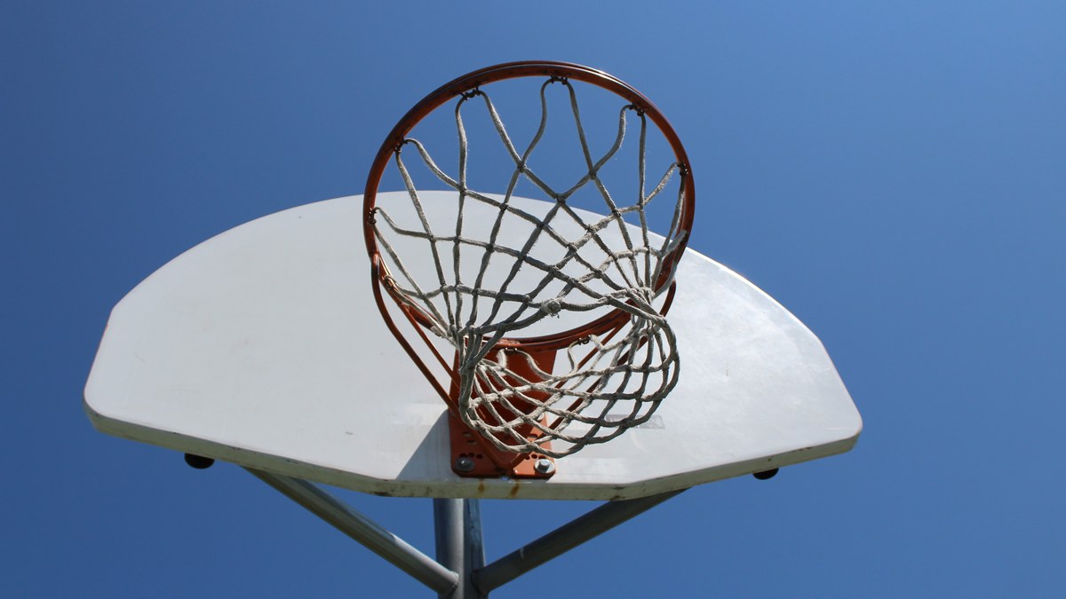 An orange basketball rim and white net viewed from below against a clear blue sky
