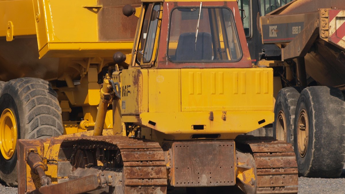 A big yellow bulldozer with a steel blade and tracks parked beside other yellow construction machines on a gravel lot