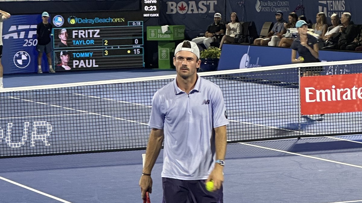 American tennis player Tommy Paul in a light blue shirt and white cap holding a tennis ball on court