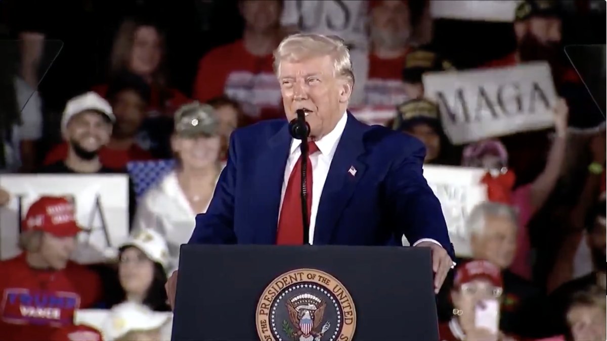 President Donald Trump speaks at a podium bearing the presidential seal in front of a cheering rally crowd