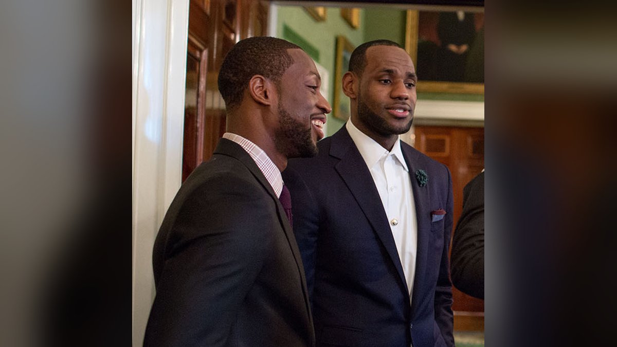 LeBron James smiling in a navy suit beside Dwyane Wade during a White House visit in January 2014