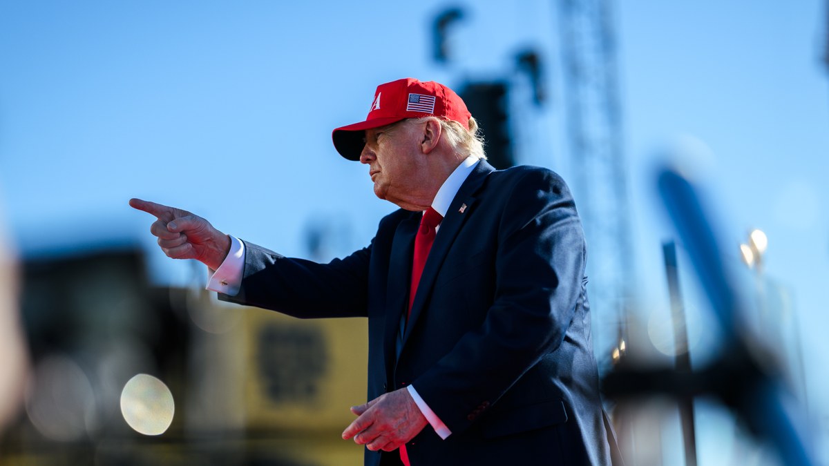 Donald Trump in a red cap pointing from an outdoor stage