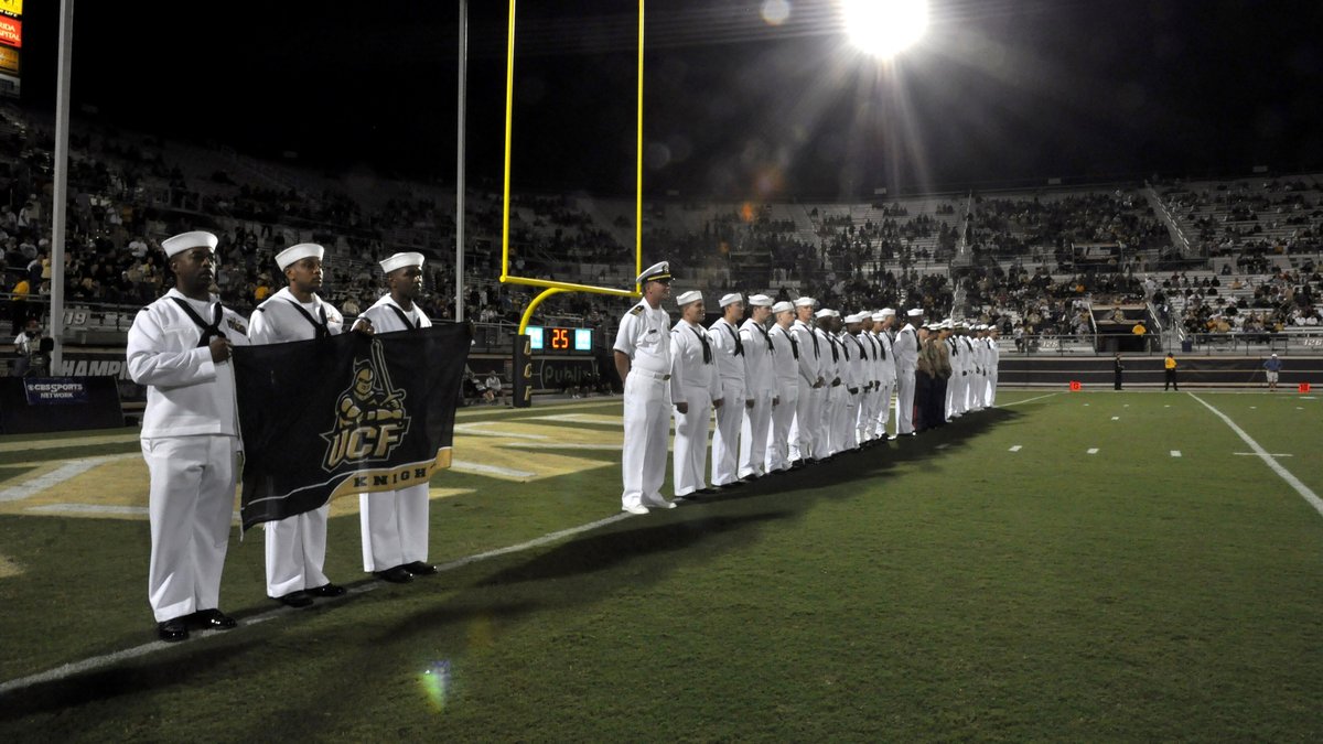 Sailors standing in a line on the field under the stadium lights during a UCF Knights home football game in Orlando