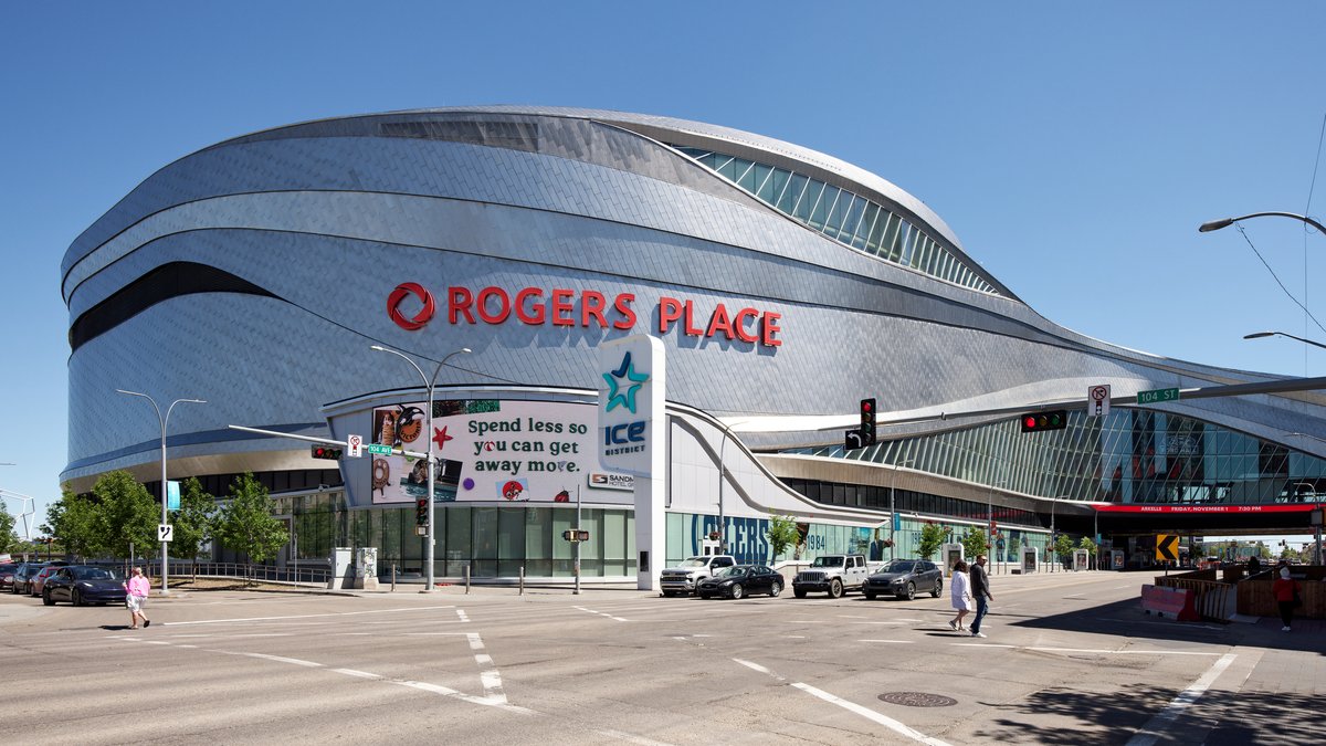 The silver curved exterior of Rogers Place arena in Edmonton with red ROGERS PLACE lettering under a clear sky