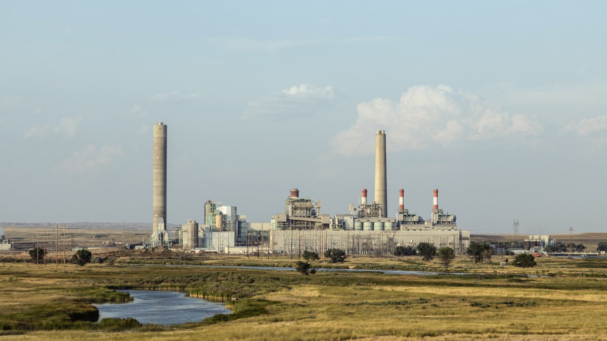 Two tall smokestacks rise over a coal-fired power plant beyond a wide prairie and a small pond in Wyoming