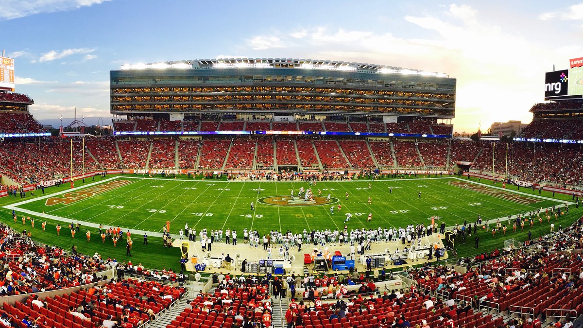 A wide view of Levi's Stadium in Santa Clara, California, with fans in red seats ringing the field under a sunset sky