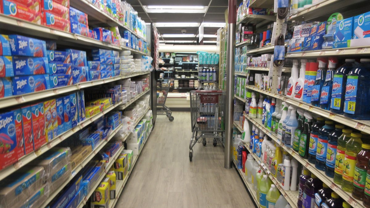Long grocery store aisle lined with shelves of paper towels, detergent and cleaning supplies
