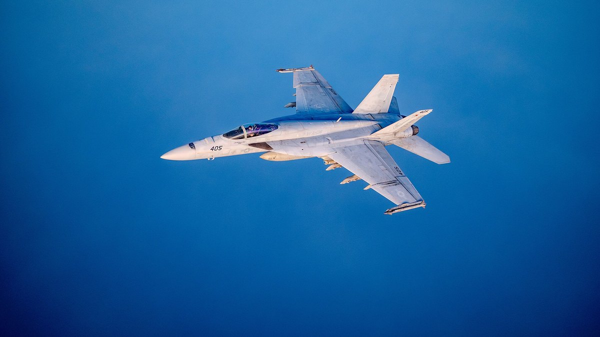 A U.S. Navy F/A-18 Super Hornet fighter jet flying against a deep blue sky
