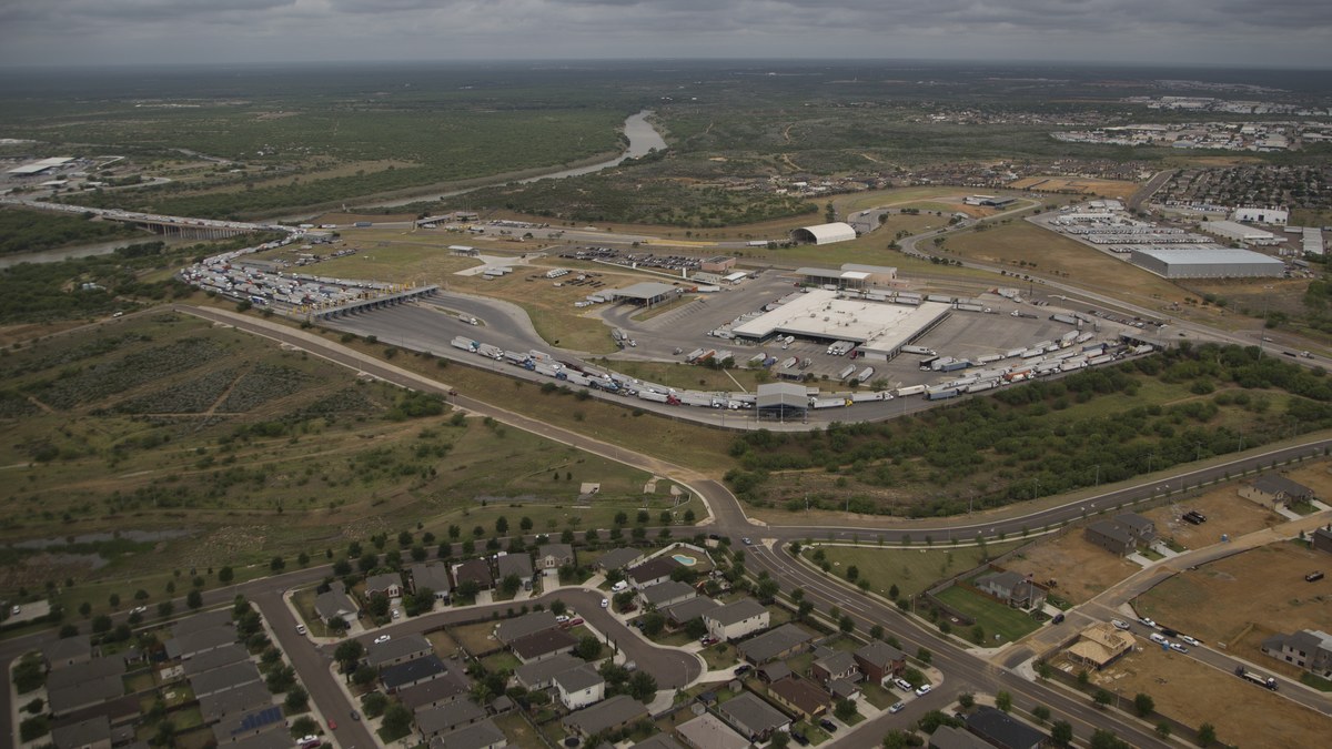 Aerial view of commercial trucks lined up at the World Trade Crossing bridge between Laredo Texas and Mexico beside the Rio Grande