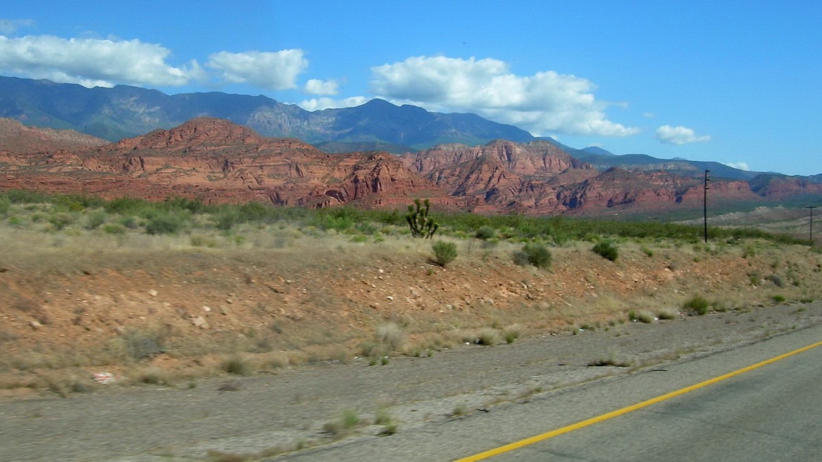 Interstate 15 running past red rock cliffs and desert brush in southern Utah under a blue sky