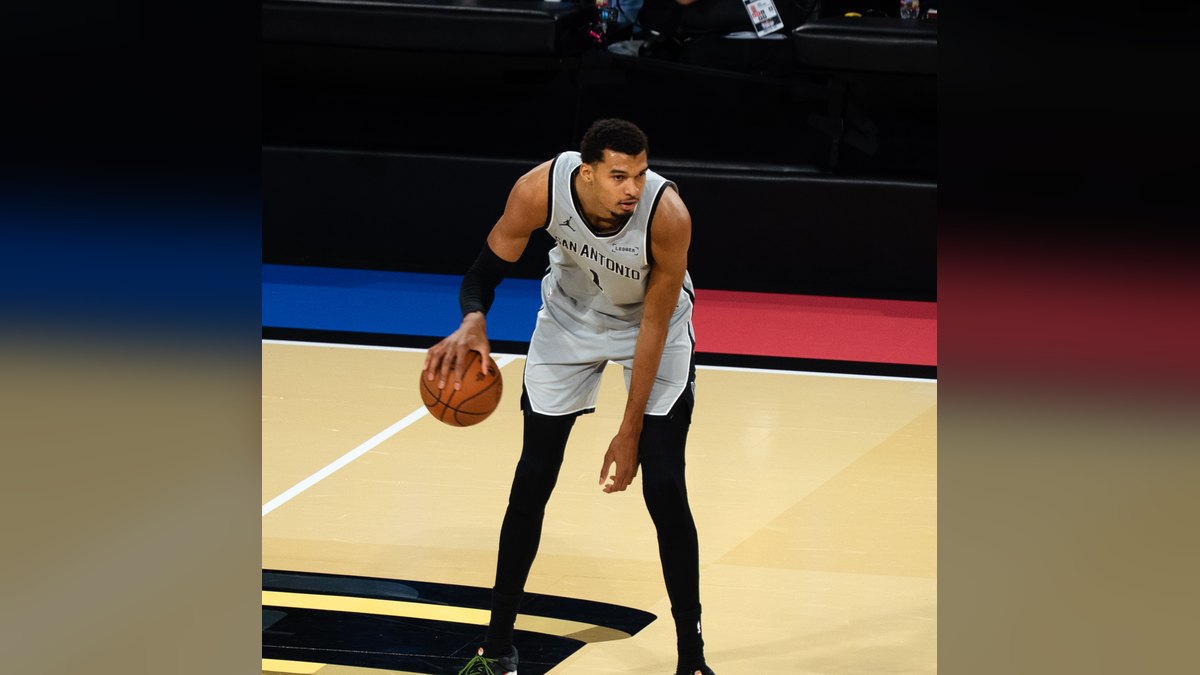 Victor Wembanyama in a white San Antonio Spurs uniform dribbling the ball near the 3-point line