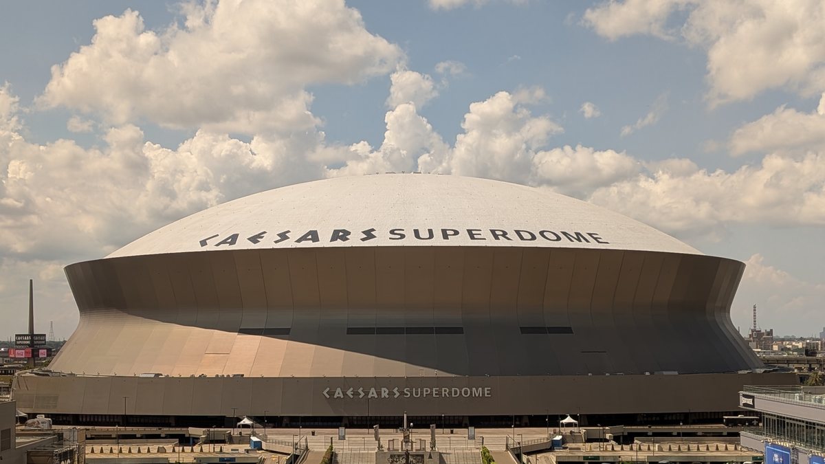 The domed roof of the Caesars Superdome in New Orleans under a partly cloudy sky